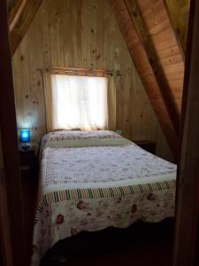 Cama en una cabaña de madera con ventana en Cabaña en Choshuenco con Tinaja, en Choshuenco