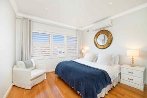 a white bedroom with a bed and a chair at Beach-Front Apartments in Sydney