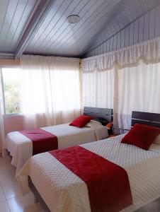 a bedroom with three beds with red and white sheets at Hostal el Parque Tababela in Tababela