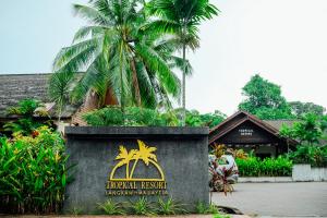 a sign for a tropical resort with palm trees in the background at Tropical Langkawi in Pantai Cenang