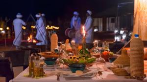 a table with food and wine bottles and candles on it at Luxurious Merzouga Desert Camps in Merzouga