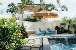 a pool with two blue chairs and an umbrella at Sunset Serenity Beach House in Iba
