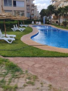 a swimming pool with white lounge chairs and an umbrella at Bel appartement pour location in O Ben Slimane