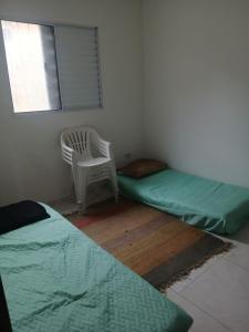 a room with two beds and a chair and a window at Apartamento na praia 2 qt com quintal e churrasqueira in Itanhaém
