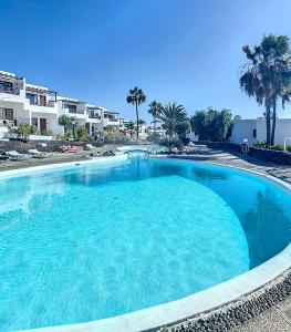 a large blue swimming pool with palm trees and buildings at Tabaiba Place in Tías