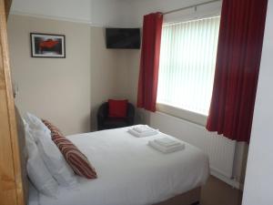 a bedroom with a white bed with red curtains and a window at Clinmore House in Paignton