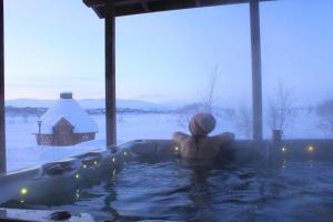 a man sitting in a hot tub in a snow covered yard at Tundrea Holiday Resort in Kilpisjärvi