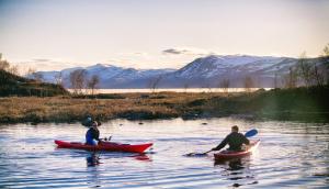 three people kayaking on a river with mountains in the background at Tundrea Holiday Resort in Kilpisjärvi