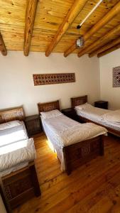 a room with three beds and a wooden ceiling at Nurata Eco Guesthouse in Yangiqishloq