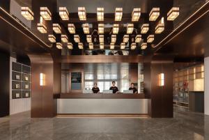 Atour Hotel Shanghai Jing'an North XIzang Road Metro Station في شانغهاي: لوبي فيه ثلاث اشخاص جالسين في كونتر