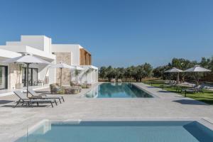a pool with chairs and umbrellas next to a building at Olive Sun Villa Stillness & Elegance by etouri in Kato Gouves +35 photos