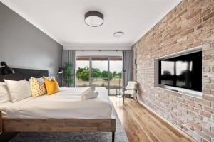 Cette chambre est dotée d'un mur en briques, d'un lit et d'une télévision. dans l'établissement Amaroo - Luxe Hinterland Three-bedroom Farmhouse with Studio, à Quindalup