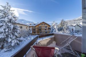 a red chair on a balcony with snow covered trees at Chesa Pradatsch Suot 5 - Celerina in Celerina