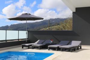 a swimming pool with lounge chairs and an umbrella at A&M House in Arco da Calheta