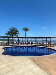 a large swimming pool next to a beach with palm trees at Golden Lake Apart Hotel in Arraial do Cabo