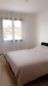 a white bed in a room with two windows at Jolie maison, plain-pied à Dole in Dole