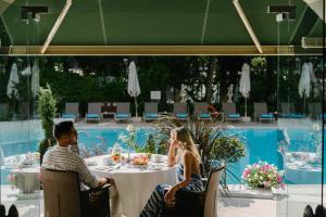 a man and woman sitting at a table in front of a pool at Rodos Park - Small Luxury Hotels of the World in Rhodes Town