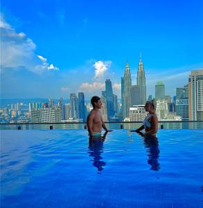 Un hombre y una mujer sentados en una piscina infinita con el horizonte de la ciudad. en The Luxe Colony KLCC by Rsafa, en Kuala Lumpur