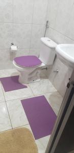 La salle de bains est pourvue de toilettes et de tapis violets. dans l'établissement Pousada Conquista do Paraíso, à Alto Paraíso de Goiás