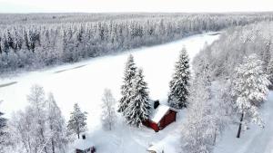 een rode hut in de sneeuw naast een met sneeuw bedekt bos bij Lapland Aurora Riverside in Raiskio
