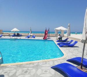 a swimming pool with blue chairs and umbrellas on the beach at فيلا لؤلؤة كرير عائلات فقط أو بنات in Sidi Kirayr