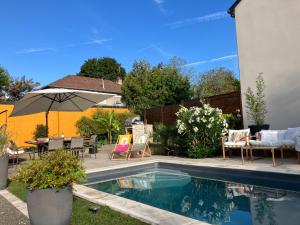 a backyard with a pool with chairs and an umbrella at Parenthèse de rêve - Piscine & confort au Mans in Coulaines