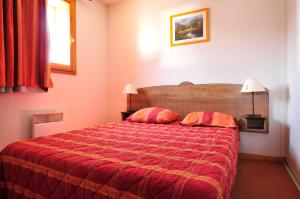una camera con letto rosso e 2 cuscini di Résidence Goélia Les Chalets de la Toussuire a La Toussuire