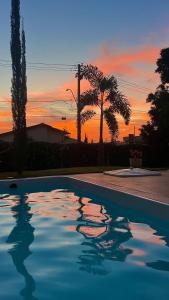 a swimming pool with a sunset in the background at Recanto Manga da Rosa - casinha de fazenda no centro da cidade in Olímpia