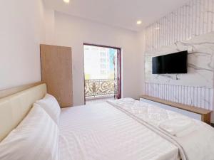 a white bedroom with a bed and a flat screen tv at Villa Thái An in Phan Thiet