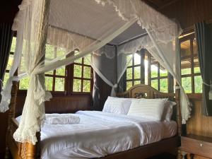 una camera da letto con letto a baldacchino con tende bianche di บ้านเอื้องดอยแม่กำปอง a Ban Pok Nai