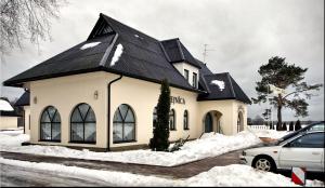 a white house with a black roof in the snow at Oškrogs in Ķegums