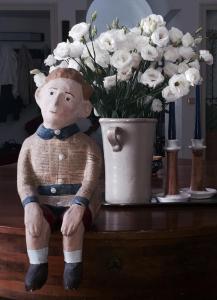 a doll sitting on a table next to a vase of flowers at Da Cristina Palazzo Atanasio in Palermo