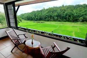 a balcony with chairs and a table and a view of a field at Vayal Veedu - Luxury Farm Villas by the woods in Muthanga