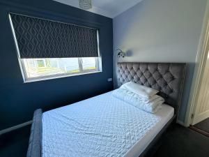 Bett in einem blauen Schlafzimmer mit Fenster in der Unterkunft Dog Friendly Chalet With Outdoor Seating At Broadland Park And Marina Ref 12050B in Lowestoft