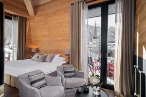 a bedroom with a bed and two chairs and a balcony at Unique Hotel Post in Zermatt