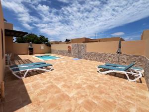 a patio with two lounge chairs and a swimming pool at Anahi Home Corralejo - Villa Cardon 12 in La Oliva