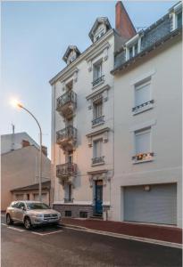 un bâtiment blanc avec une voiture garée devant dans l'établissement LE DARCET - Hypercentre - Calme - Proche Gare & Thermes, à Vichy