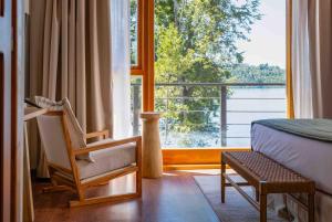 a bedroom with a bed and a chair and a large window at Puerto Manzano Boutique Hotel in Villa La Angostura