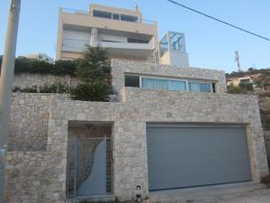 a house with a garage with a building in the background at Viva B&B in Anavyssos