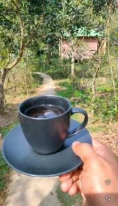 a person holding a cup of coffee on a plate at Nishorgo Nirob Eco Resort in Sreemangal +3 photos