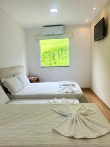 1 dormitorio con 2 camas, TV y ventana en Bik House Pousada e Festa, en Mimoso do Sul