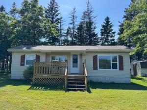 a small white house with a porch and a yard at Hidden Acres Cottages in Cavendish