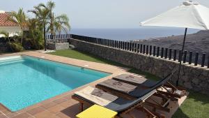 a swimming pool with two chairs and an umbrella at Villa La Pintora in Playa de Santiago