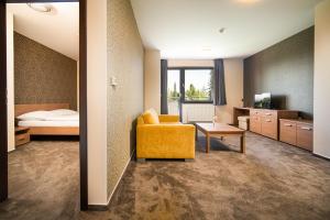a room with a yellow chair and a bed and a table at Hotel Panorama Resort in Štrbské Pleso