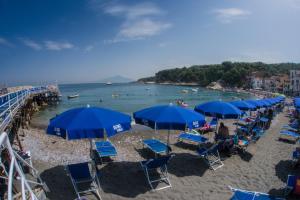 a beach with blue umbrellas and people in the water at Hotel Baia Di Puolo in Massa Lubrense