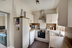 une cuisine avec des armoires blanches, un évier et un réfrigérateur dans l'établissement Dottys Cottage, à Blakeney