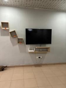a flat screen tv on a white wall with shelves at Residence Cloé in Ouagadougou