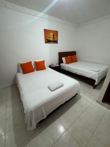 two beds in a room with white walls and orange pillows at Hotel De La Prada in Maicao +46 photos