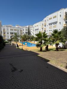 a resort with a pool and palm trees and a building at Appartement tangier airport in Hajreien