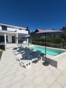 a group of lawn chairs and umbrellas next to a pool at Villa Kally in Velika Remeta